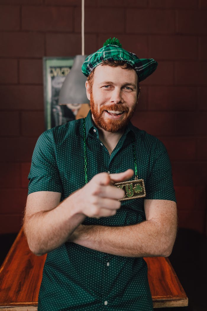 Smiling man in a green shirt and cap points indoors, embracing festive cheer.